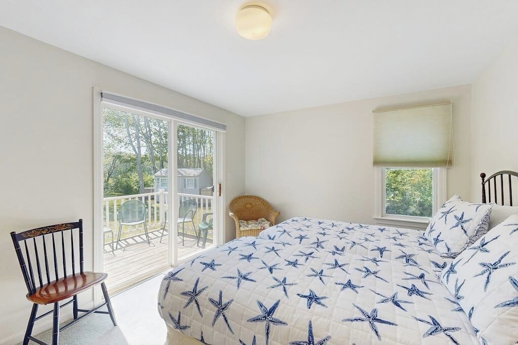 A bedroom with a large bed, a chair, a window, and a view of the outdoors.