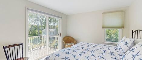 A bedroom with a large bed, a chair, a window, and a view of the outdoors.