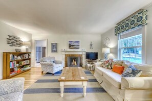 Ein Wohnzimmer mit Kamin, Sofa, Sessel und Bücherregal.