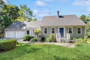 A two-story house with a garage, a front porch with a table and chairs, and a well-maintained lawn. - Charming  Retreat w/ WiFi, Ping Pong Table & Walking Distance to the Ocean (Cumberland)