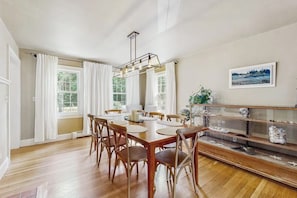 A dining room with a wooden table, chairs, a chandelier, and a display case with decorative items. - Charming  Retreat w/ WiFi, Ping Pong Table & Walking Distance to the Ocean (Cumberland)