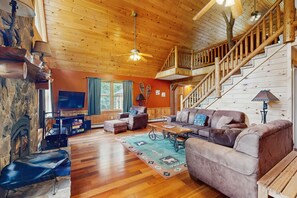 A cozy cabin interior with a wooden staircase, a fireplace, and a comfortable seating area.
