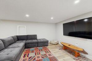 A modern living room with a sectional sofa, a flat-screen TV, a wooden bench, and a colorful rug.