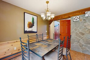 A dining area with a wooden bench, a table with a patterned tablecloth, and a chandelier.