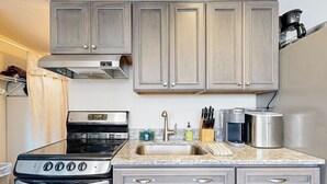 A kitchen with grey cabinets, a stainless steel stove, a sink, and a coffee maker. - Cozy Studio with Slopeside Access, Pool, Sauna, and Mountain Views (Newry)