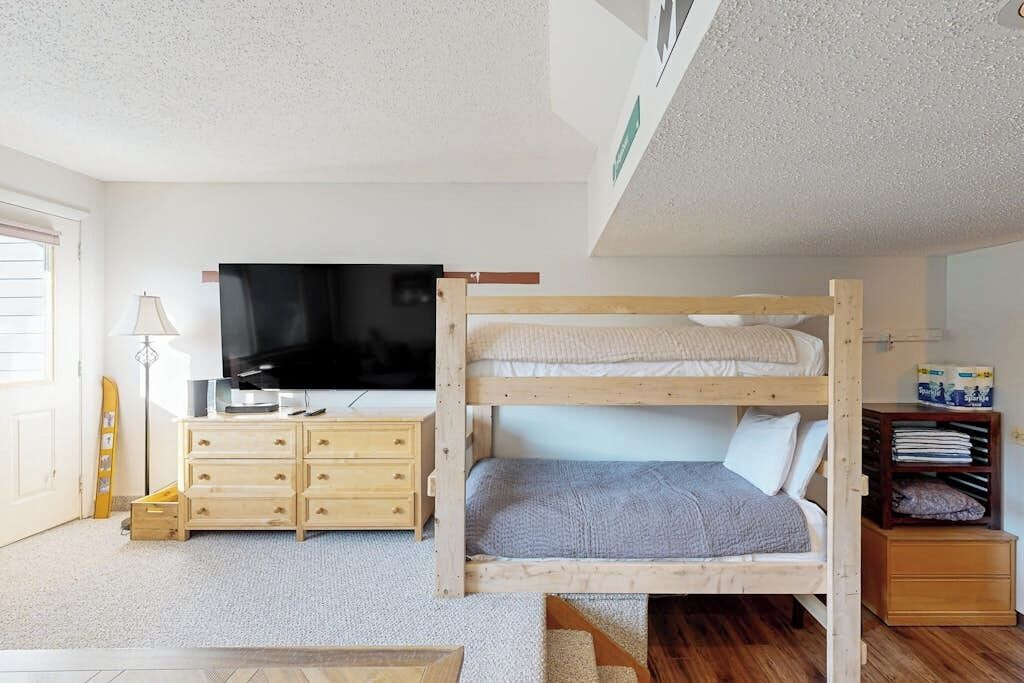 Un lit superposé avec une télévision, une commode en bois et une étagère remplie d’objets.