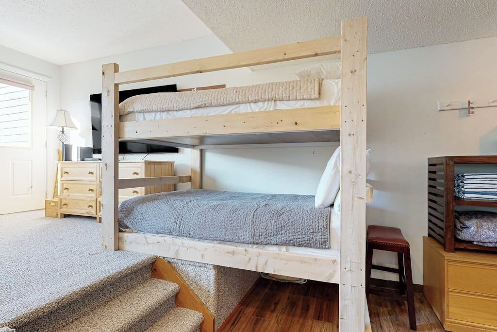 Een stapelbed met bureau en lades, betegelde trap en een houten kruk.