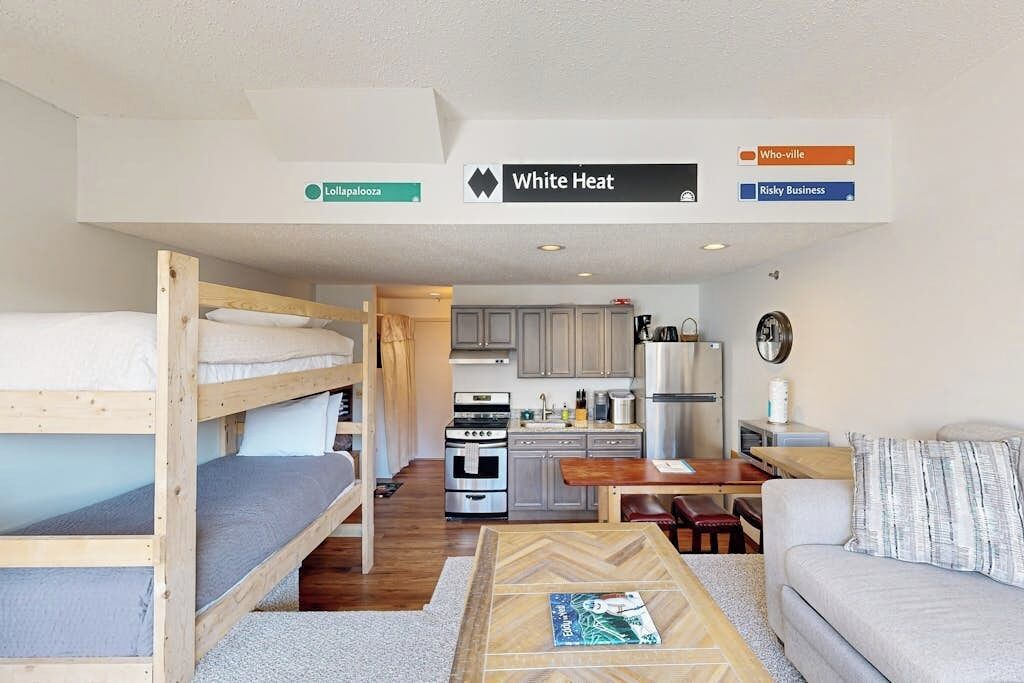 A bunk bed, kitchenette, dining area, and a sofa in a room.
