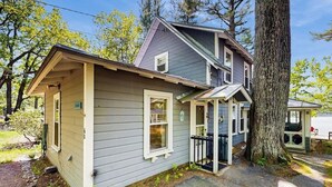 Ein zweistöckiges Haus mit einer überdachten Veranda, einer kleinen angeschlossenen Garage und einem großen Baum davor.