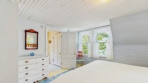 Ein Schlafzimmer mit einem Bett, einem Schminktisch, einem Stuhl und einem Fenster mit Vorhängen.