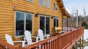 A wooden cabin with a porch, white Adirondack chairs, and a red railing.