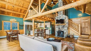 A spacious living area with a stone fireplace, wooden ceiling beams, and a dining area with a large window.