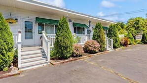 Un motel blanc avec un auvent vert, une véranda et un parking.