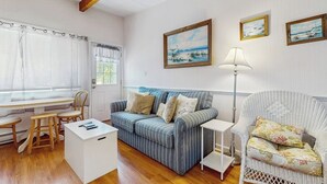 Une pièce avec un canapé à rayures, un fauteuil blanc, une petite table et une fenêtre avec des rideaux.