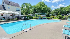 Une piscine dotée d’un espace abrité, de chaises longues et d’une maison à l’extérieur blanc.