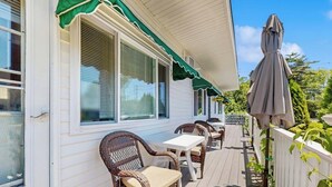 Une véranda couverte avec des meubles en osier, une clôture blanche et un auvent vert.