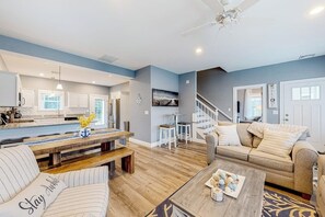 Ein modernes Wohnzimmer mit einer Küche im Hintergrund, einer Holzbank, einem Sofa und einem Couchtisch.