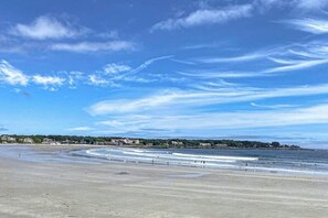 Ein Strand mit blauem Himmel, Wellen und einer fernen Küste mit Gebäuden.