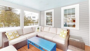 En inglasad veranda med en modulsoffa, ett blått soffbord och stora fönster.