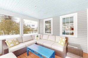 Eine überdachte Veranda mit einem Ecksofa, einem blauen Couchtisch und großen Fenstern.
