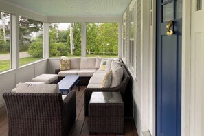 Eine überdachte Veranda mit Korbmöbeln, einem blauen Tisch und einer blauen Tür.