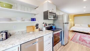 Una cocina compacta con microondas, horno y refrigerador, una tabla de cortar de madera y un juego de cuchillos.