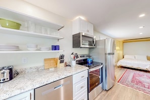 A compact kitchen with a microwave, oven, and refrigerator, a wooden cutting board, and a set of knives. - Shorelands 44-2 | Condo in Kennebunk (Kennebunk)