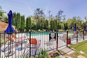 A fenced outdoor pool area with lounge chairs and umbrellas, surrounded by trees. - Shorelands 44-2 | Condo in Kennebunk (Kennebunk)