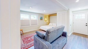 Un dormitorio con cama, un sofá gris, un tapete rojo, una ventana y una puerta.