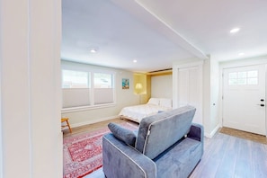A bedroom with a bed, a grey sofa, a red rug, a window, and a door. - Shorelands 44-2 | Condo in Kennebunk (Kennebunk)