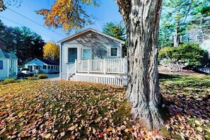 A small, single-story house with a porch, surrounded by trees and a lawn covered with fallen leaves. - House with central A/C, pool table and patio, a short drive to Little Beach (Ogunquit)