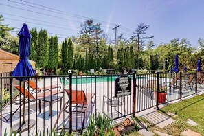 A fenced outdoor pool area with lounge chairs and umbrellas, surrounded by trees.