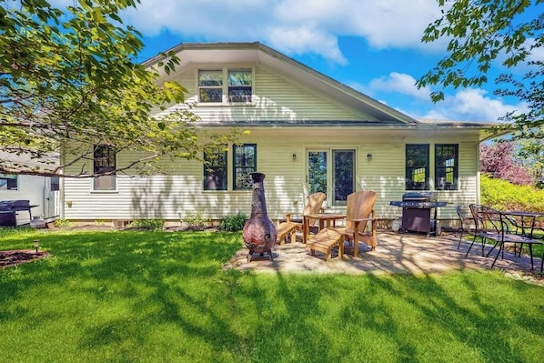 A house with a covered patio, outdoor furniture, and a large decorative urn. - Dog-friendly home with full kitchen, private W/D, & outdoor firepit (Ogunquit)