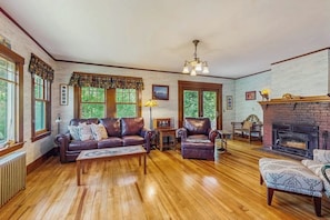 A cozy living room with a fireplace, leather furniture, and large windows. - Dog-friendly home with full kitchen, private W/D, & outdoor firepit (Ogunquit)