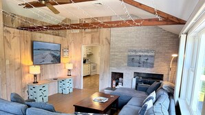 A living room with a sectional sofa, a wooden ceiling, a fireplace, and a kitchen in the background. - Spacious home near water, and walk to iconic Ogunquit beach (Ogunquit)