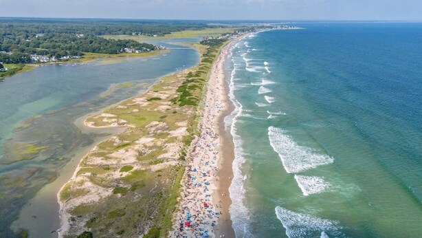 An aerial view of a coastal beach with a long stretch of sand, a clear blue sea, and a distant shoreline with buildings. - Spacious home near water, and walk to iconic Ogunquit beach (Ogunquit)