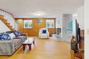 Ein Wohnzimmer mit Sofa, Sessel, Kamin und einer Holztreppe.