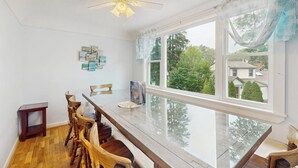 A dining area with a long wooden table, chairs, a ceiling fan, and a large window with curtains. - Spacious home near water, and walk to iconic Ogunquit beach (Ogunquit)