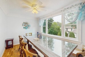 Ein Essbereich mit einem langen Holztisch, Stühlen, einem Deckenventilator und einem großen Fenster mit Vorhängen.