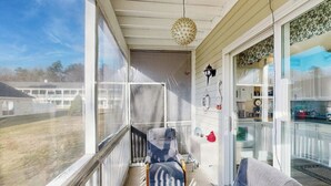 A balcony with a chair, a rug, and a hanging light fixture. - Studio condo with furnished patio, sauna, & pool - near beaches (Wells)