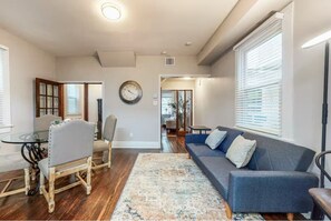 Ein Wohnzimmer mit einer Couch, einem Esstisch mit Stühlen, einem Teppich und einer Uhr an der Wand.