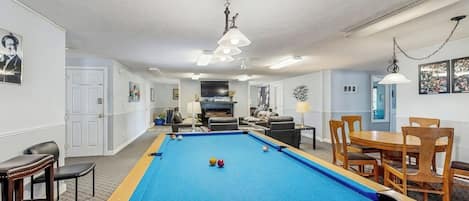 A pool table in a room with a sofa, chairs, and a dining table.