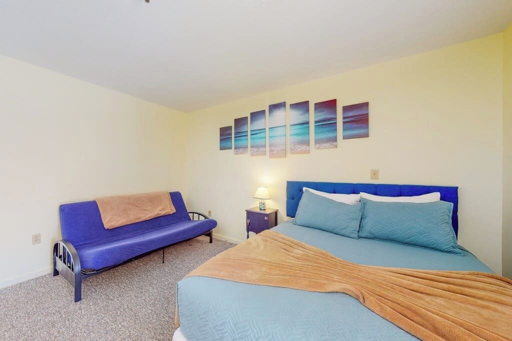 A bedroom with a bed, a blue sofa, a nightstand, and a wall with five paintings.