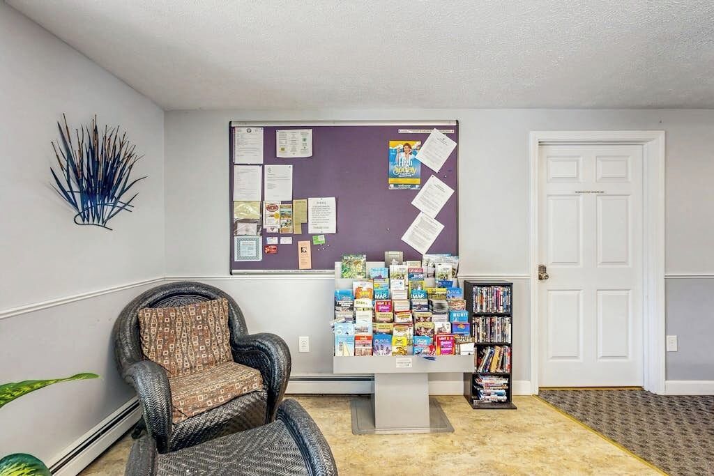 A lobby with a bulletin board, a chair, a bookshelf, and a door.