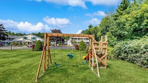 A wooden swing set in a grassy yard with houses in the background.