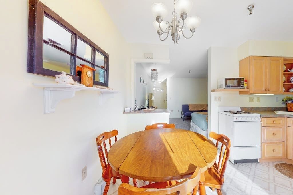 Zona pranzo con tavolo e sedie in legno, un lampadario, un forno a microonde e una stufa nell'area cucina.