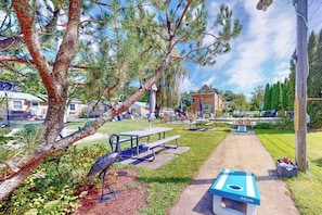 Un parc avec des tables de pique-nique, une table de jeu de GoSports et un grand arbre.