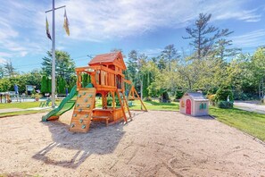 Ein Spielplatz mit einer Holz-Kletterkonstruktion und einem kleinen Gebäude.