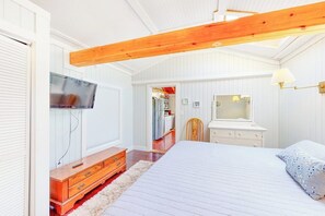 Ein Schlafzimmer mit Bett, Holzkommode, Schminktisch und Wandfernseher.