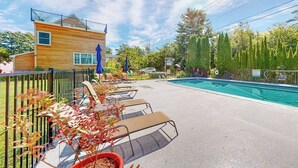 Zona de piscina con sillas de descanso, un edificio de madera y un jardín cercado.